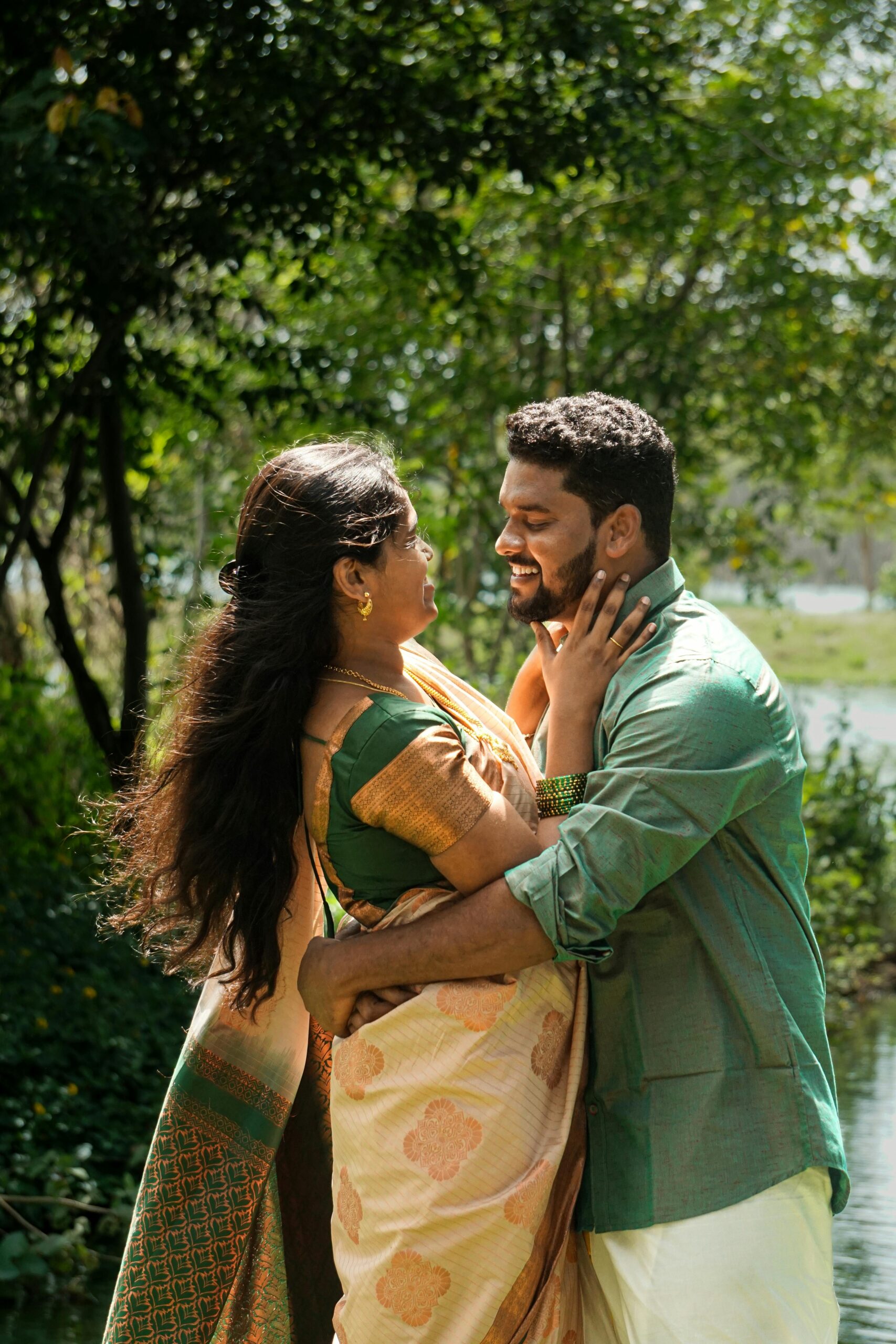 A South Asian couple sharing a joyful embrace in a serene outdoor setting.