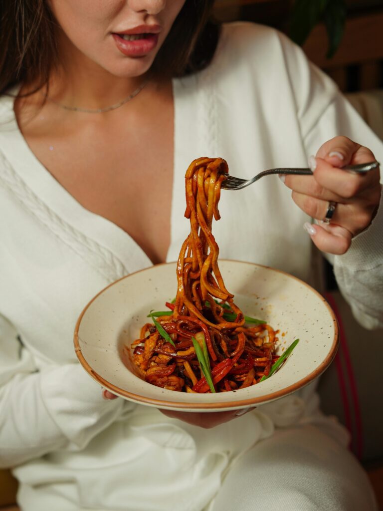 A woman in a white outfit enjoying a delicious bowl of savory noodles indoors.