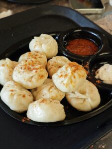 A plate of steamed momos served with spicy chutney on a black tray, perfect for a flavorful snack.