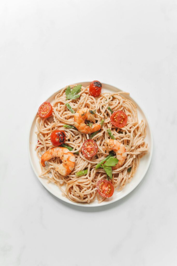 Flat lay of shrimp spaghetti with cherry tomatoes on a white plate.